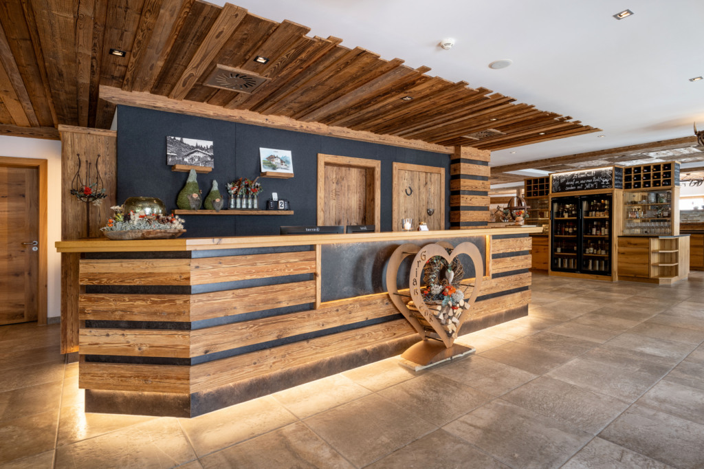 Holzverkleidete Rezeption mit dekorativem Herz und Weinregal im Hotel Sendlhof